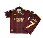 A maroon and gold Arsenal football jersey with matching shorts, displayed on a black background. The jersey features the Emirates Fly Better sponsor logo, the Adidas logo, and the Arsenal club crest.